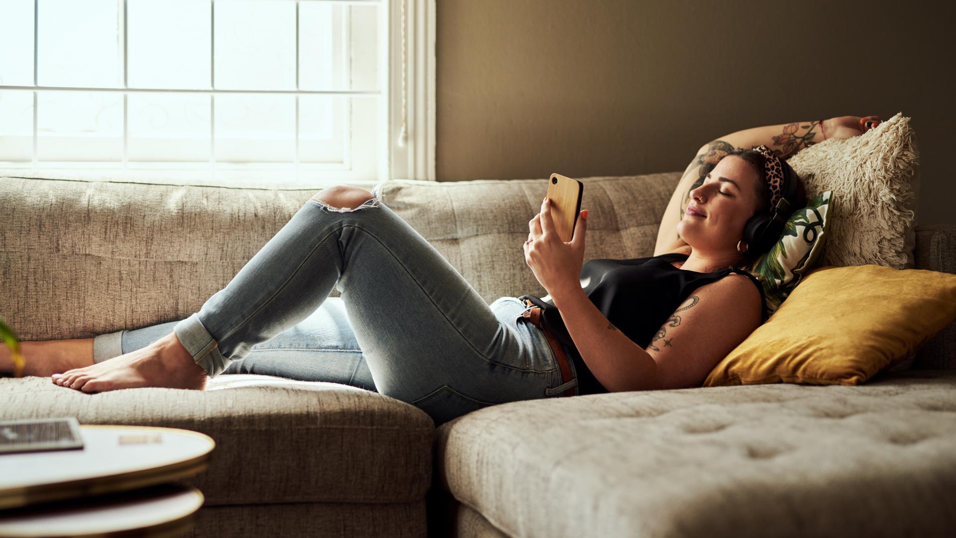 Frau entspannt am Handy liegt auf Sofa