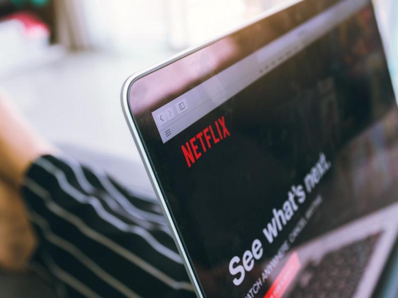 Frau mit lackierten Fingernägeln im Pyjama mit Laptop auf dem Schoß und geöffnetem Netflix-Browser offen