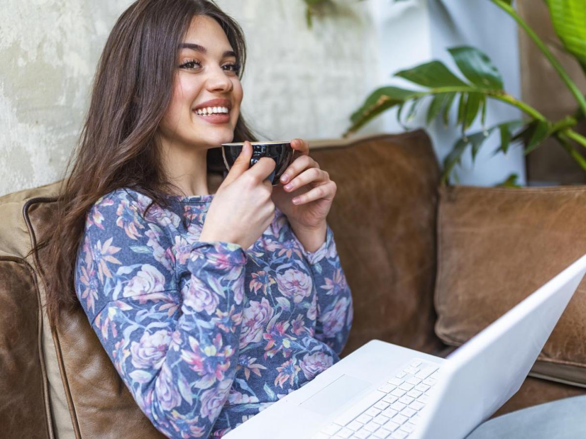 lächelnde Frau macht mit dem Laptop auf dem Schoss eine Pause