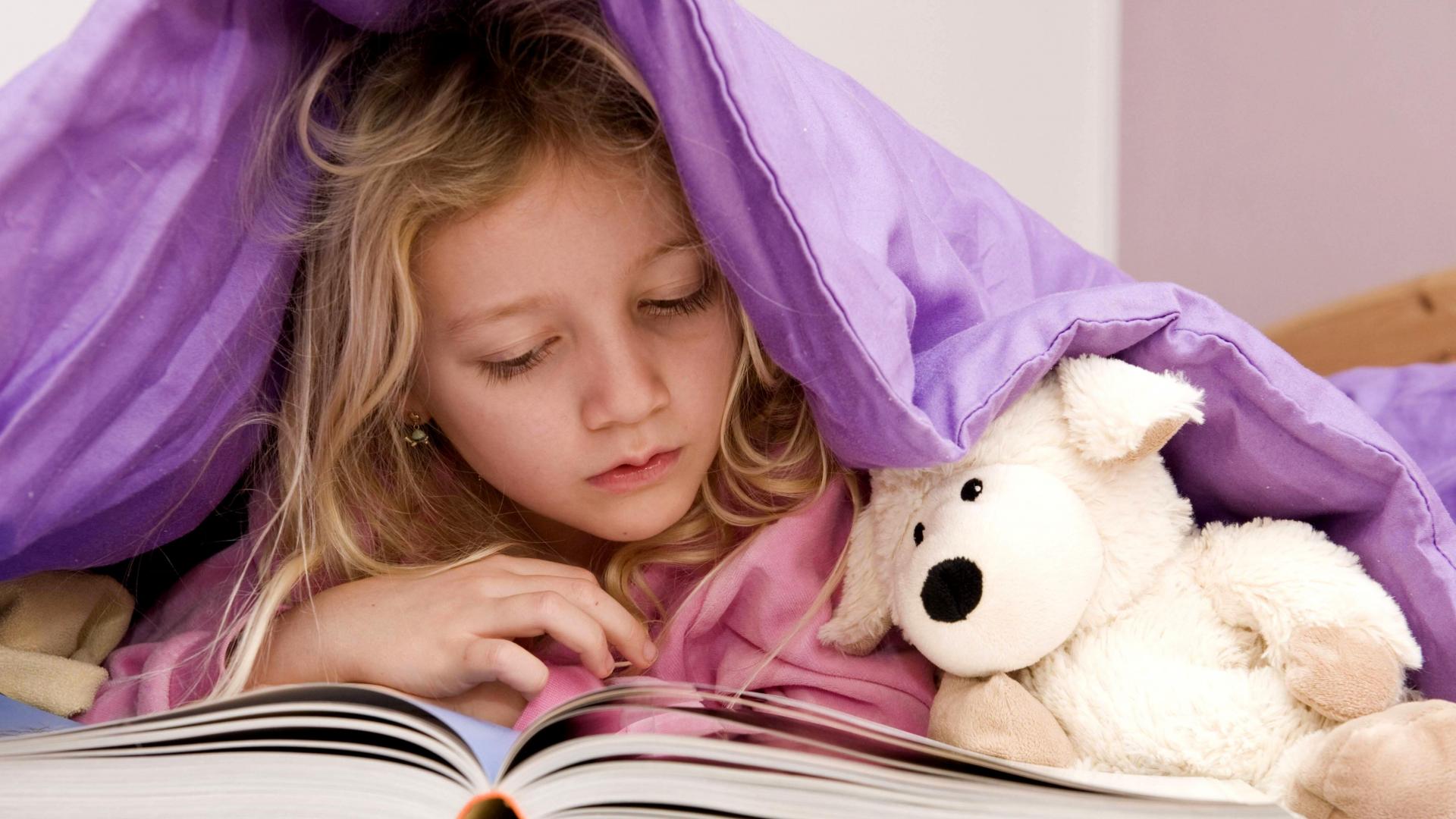 Mädchen liegt unter der Bettdecke und liest ein Buch