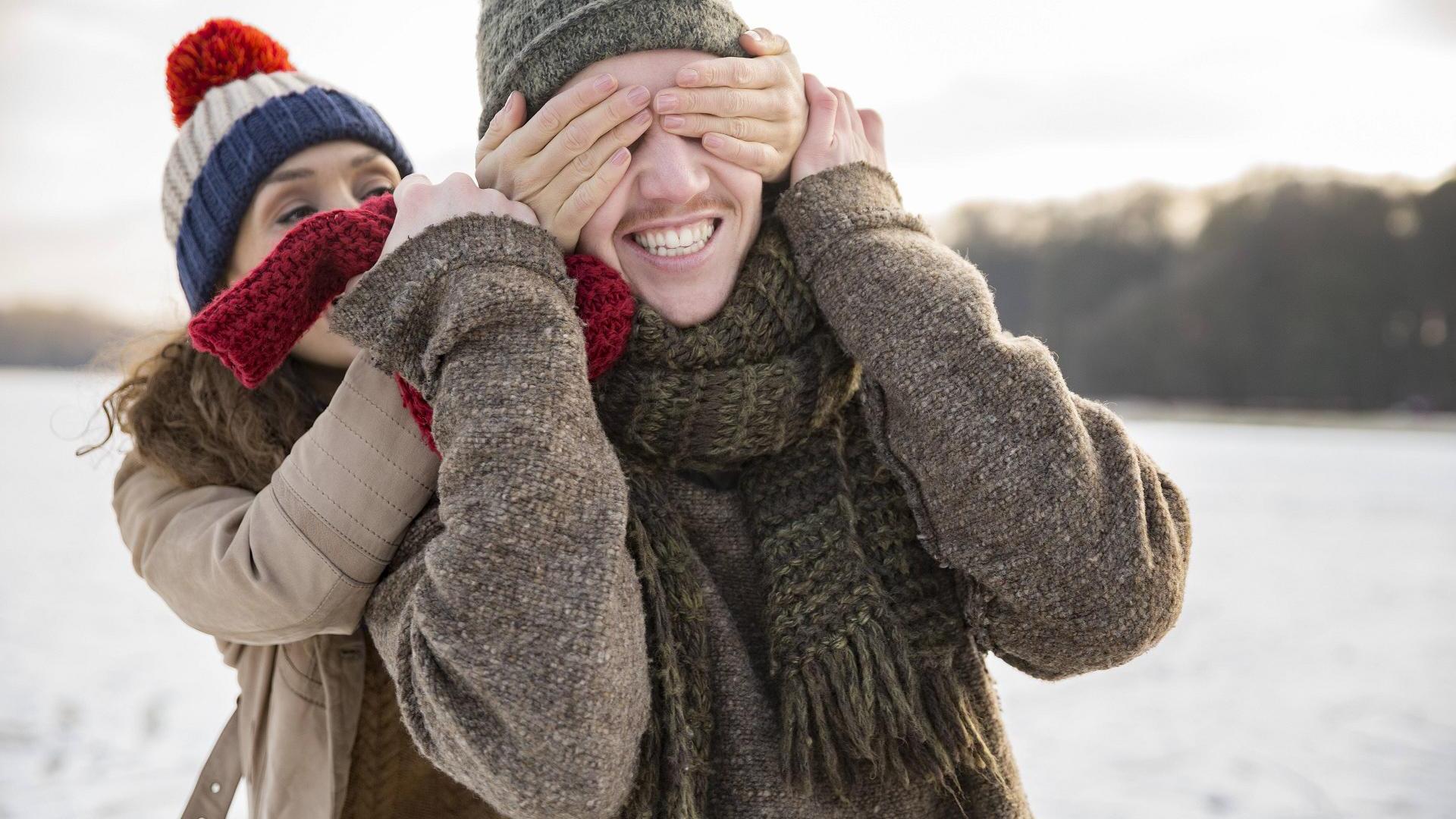 Pärchen im Winter überrascht sich, sie hält ihm die Augen zu