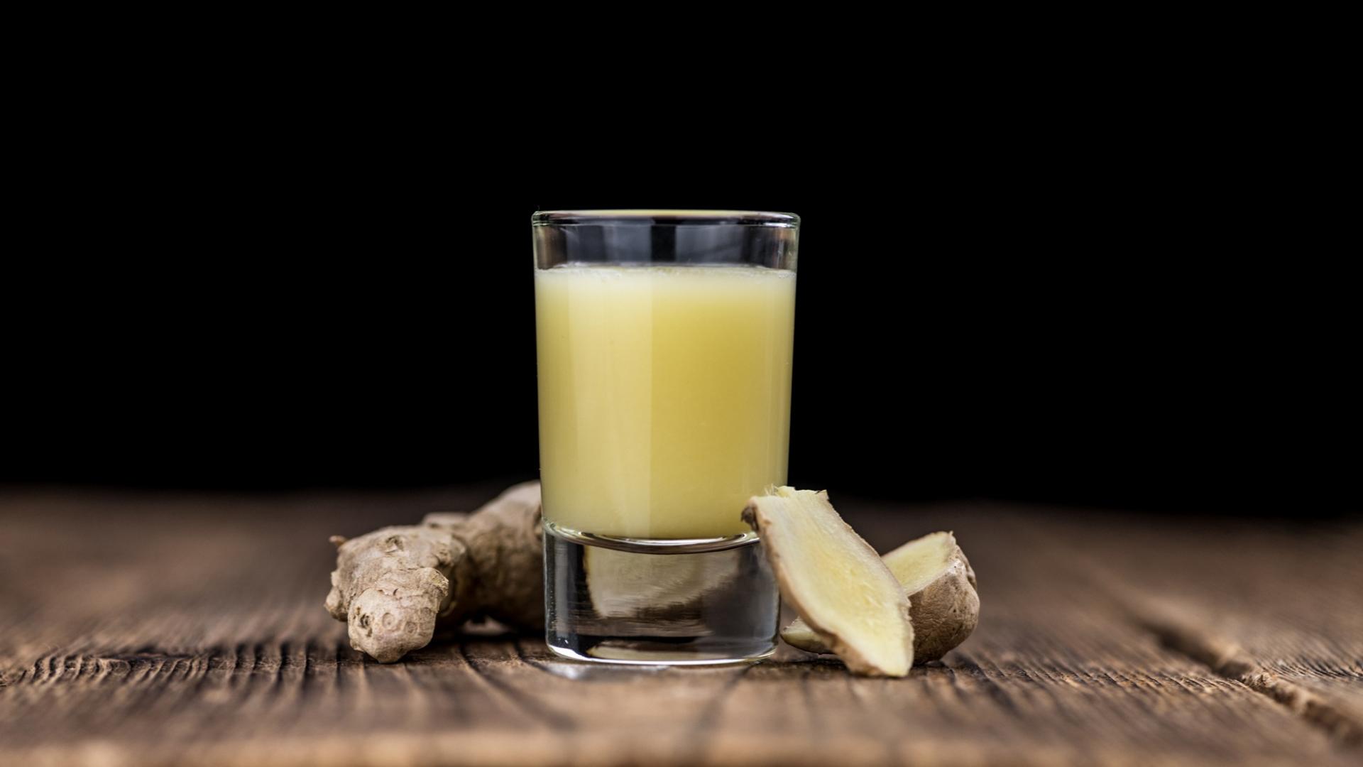 Portion Ingwer Shot in einem Shot Glas auf dem Holztisch mit einzelnen Ingwer Stücken daneben