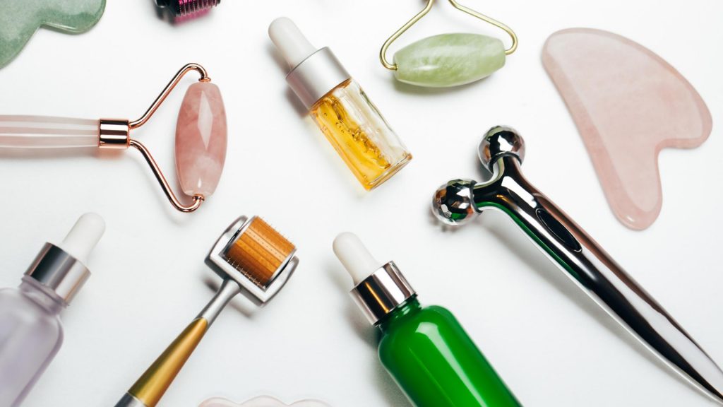 Top view of set of aromatic oils placed amidst various massage rollers and gua sha scraping tools on white background