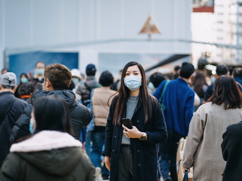 Frau mit Maske steht in Menschenmenge.