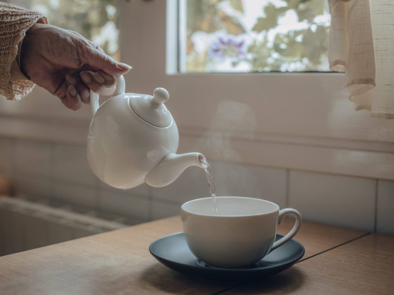 Hand gießt Tee in Tasse ein