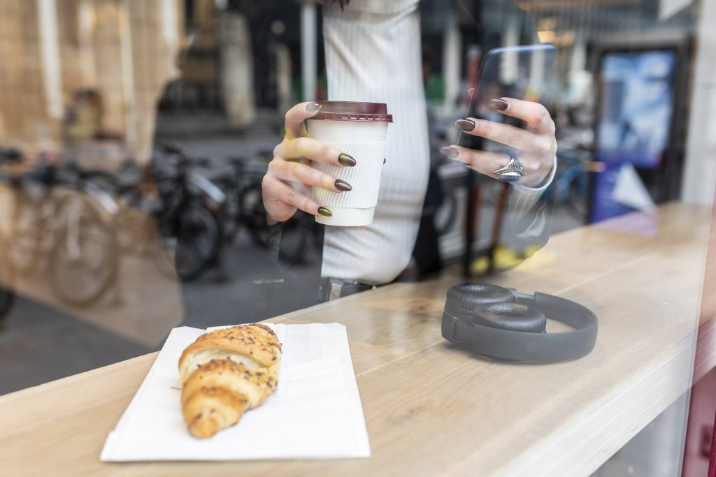 Hände mit Croissant und To Go Becher