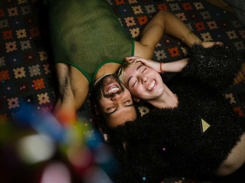 Mann und Frau liegen in einer Partyatmosphäre lachend auf einem Teppich