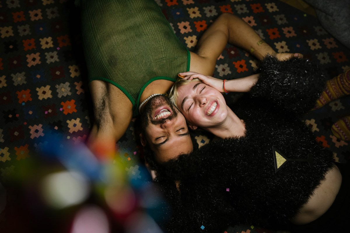 Mann und Frau liegen in einer Partyatmosphäre lachend auf einem Teppich