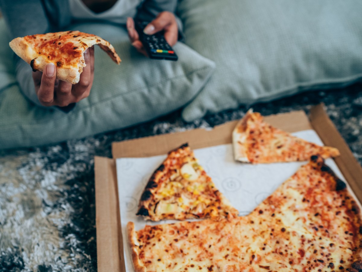 Junge Frau isst Pizza vor dem Fernseher