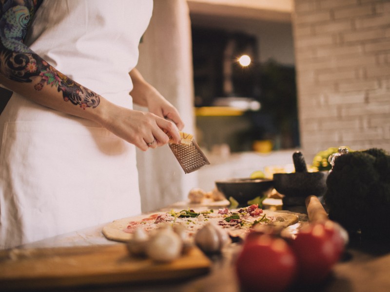 Frau streut Käse über Pizza