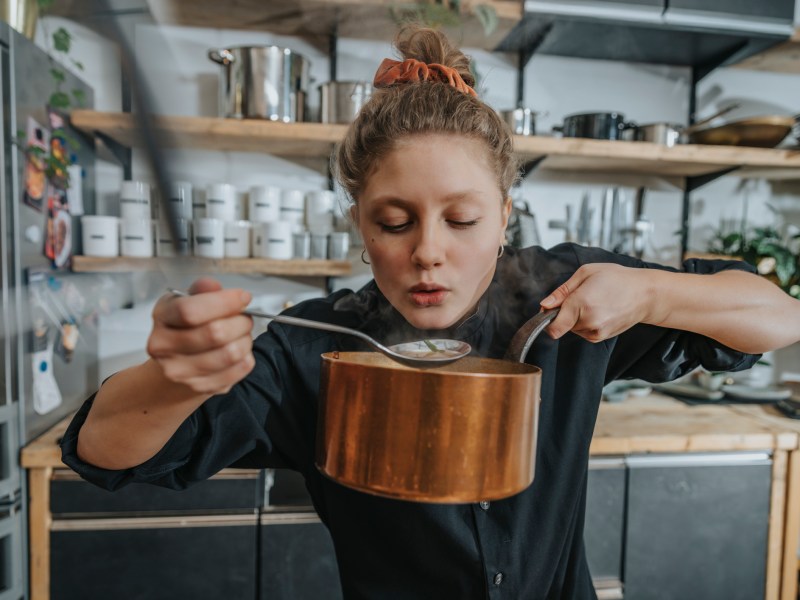 Frau probiert Suppe aus Topf