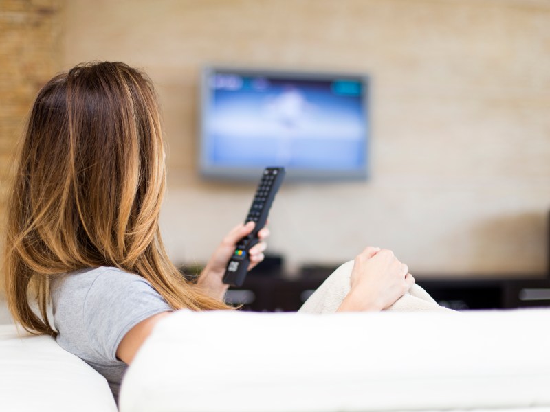 Frau hält Fernsehfernbedienung in der Hand.