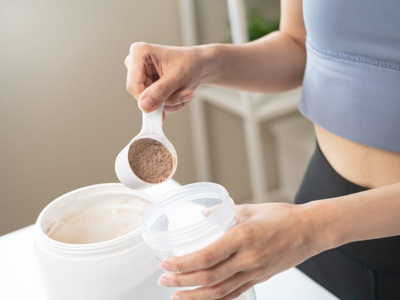 Frau gibt einen Scoop Proteinpulver in einen Shaker