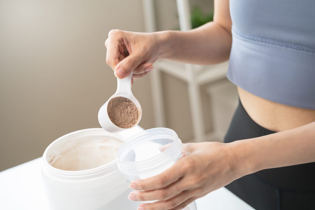 Frau gibt einen Scoop Proteinpulver in einen Shaker