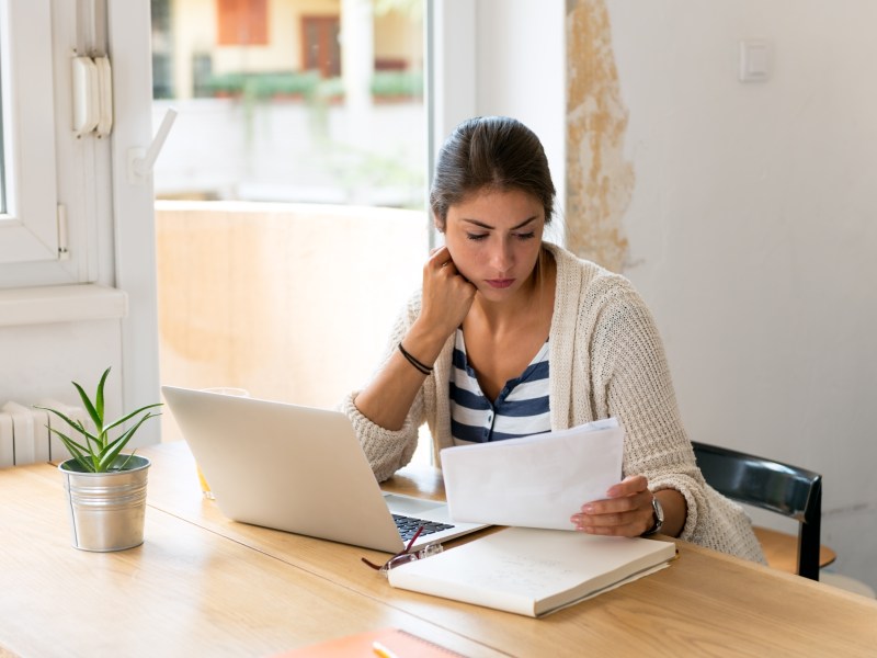 Frau schaut sich vor ihrem Laptop Unterlagen an.