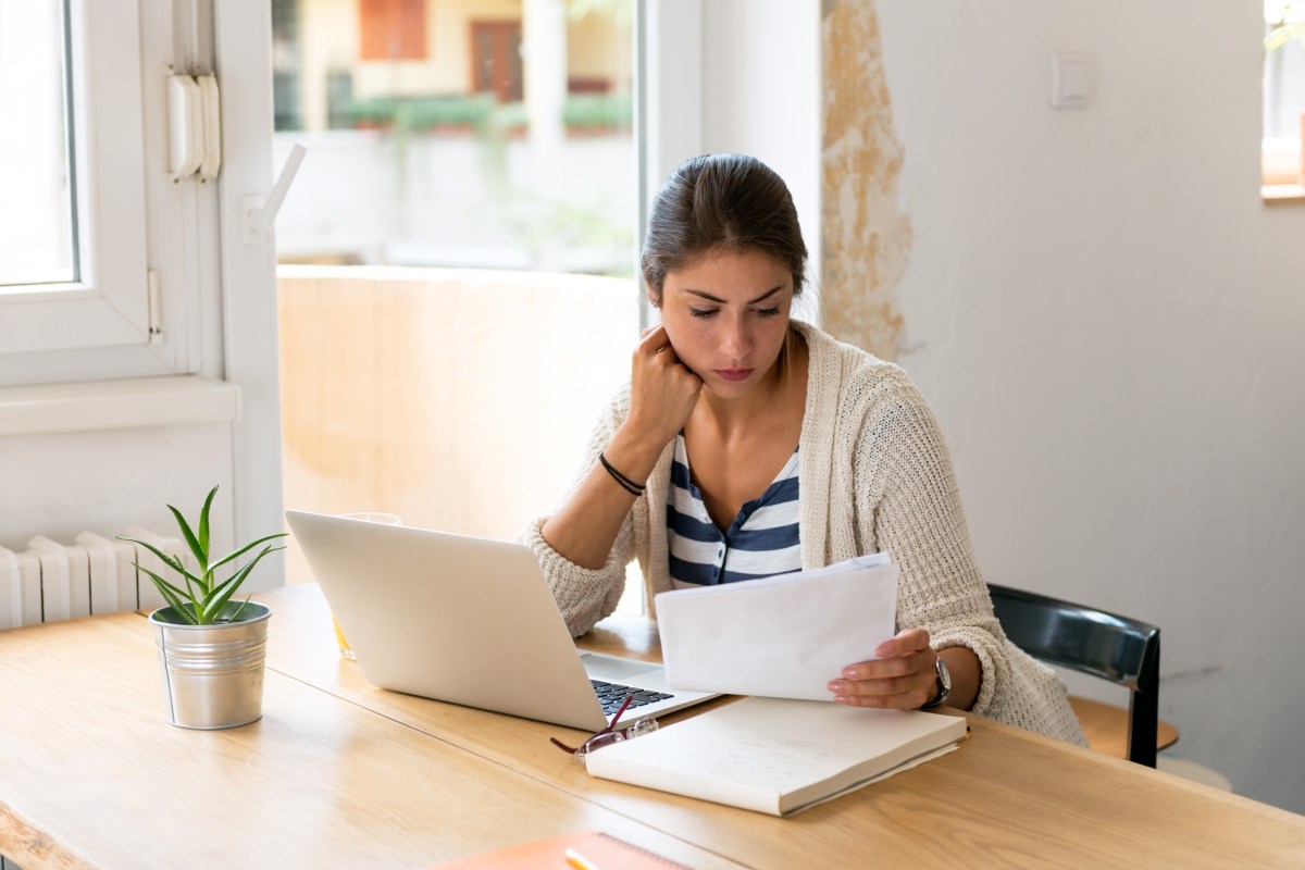 Frau schaut sich vor ihrem Laptop Unterlagen an.