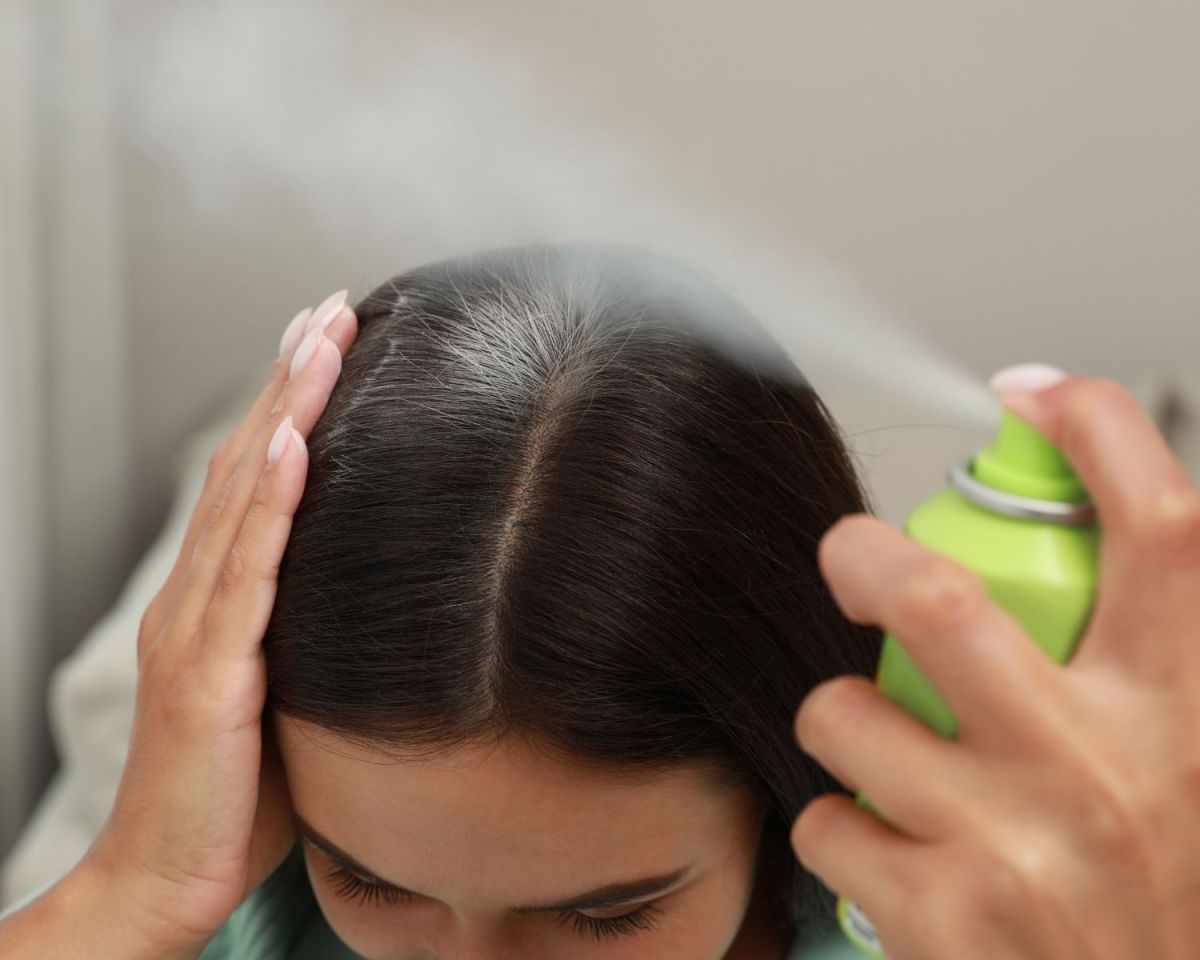 Frau sprüht Trockenshampoo auf Ansatz