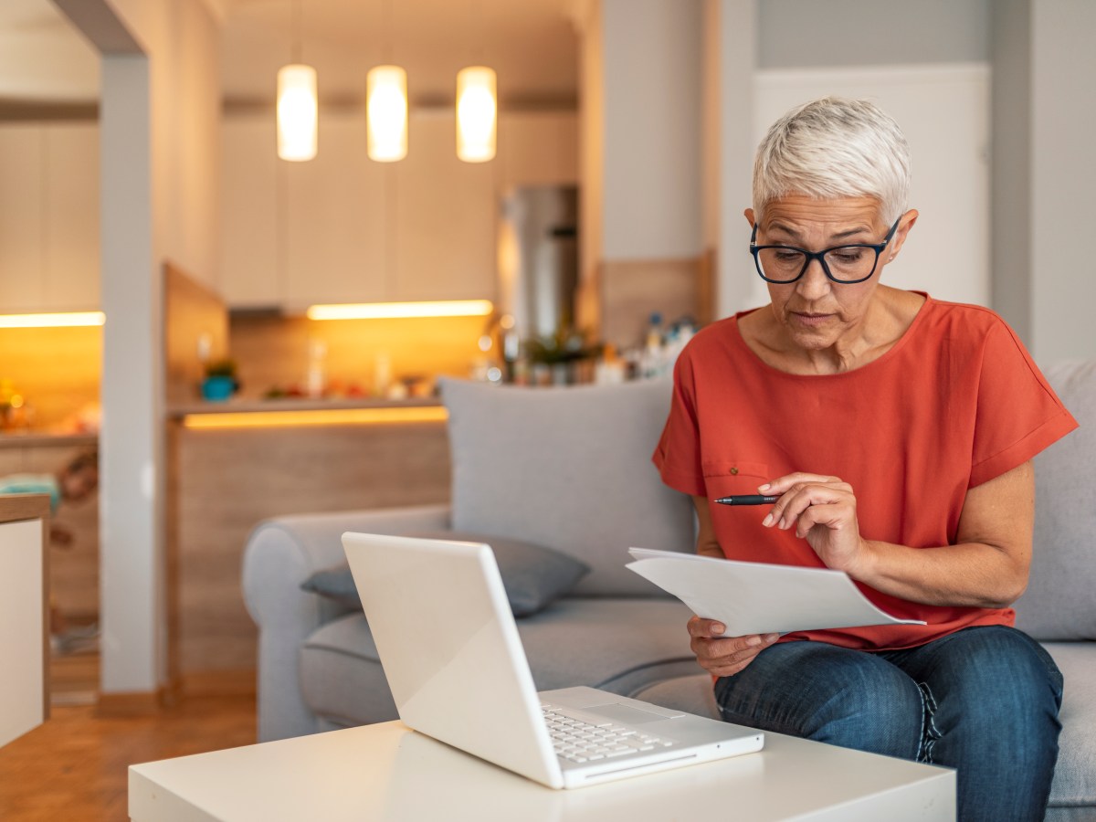 Eine Ã¤ltere Frau sitzt vor dem laptop und fÃ¼llt einen Antrag aus.