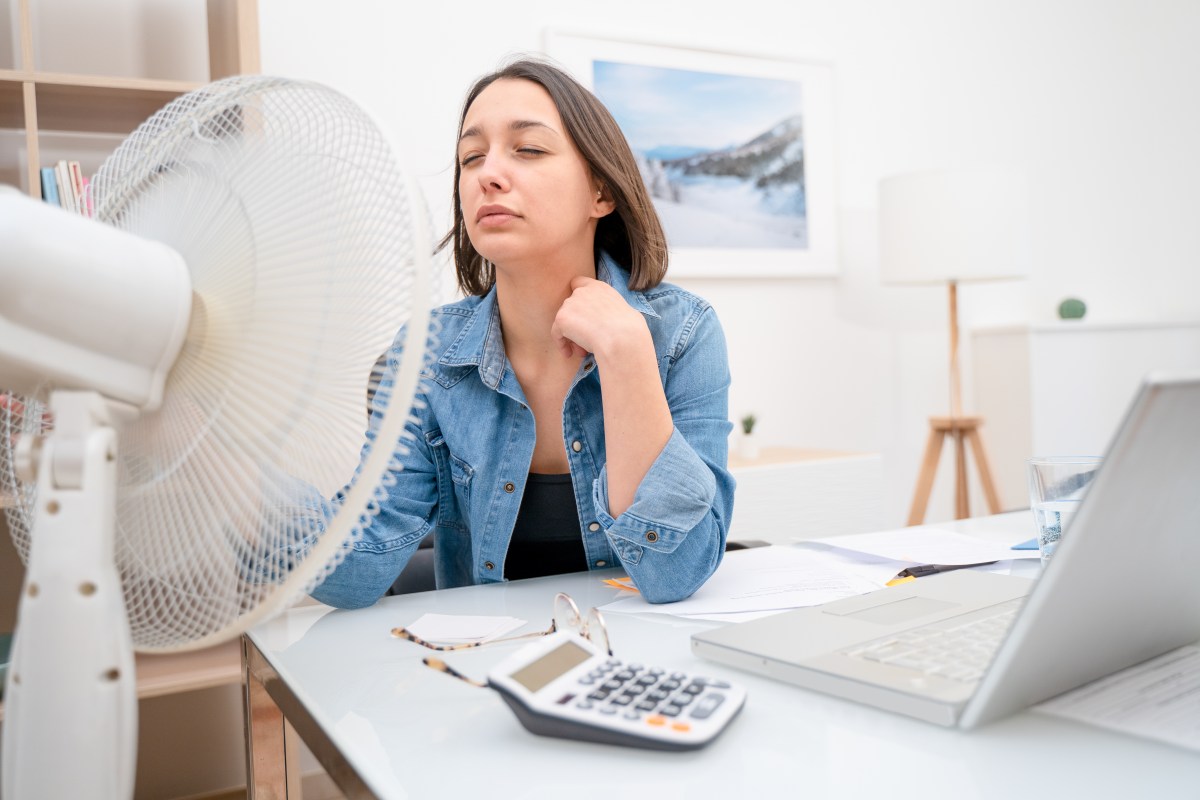 Frau sitzt mit Ventilator vor dem Laptop.