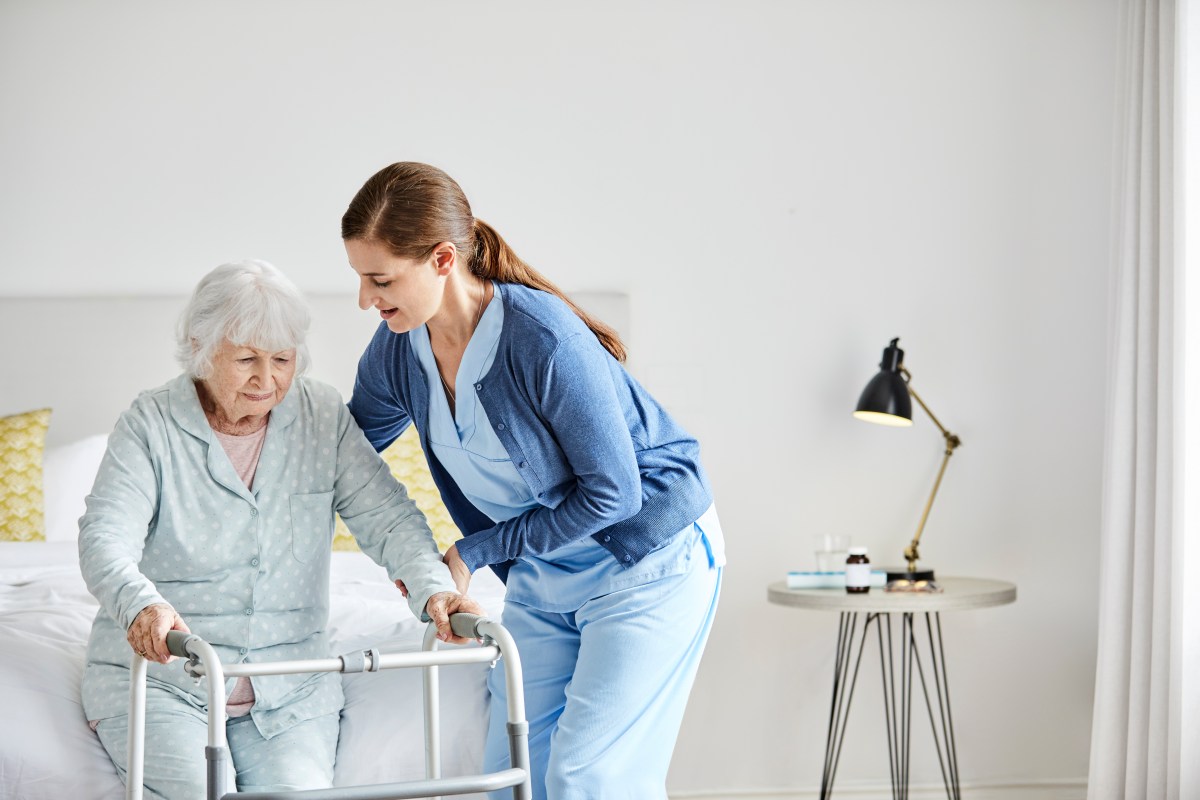 Pflegekraft hilft einer älteren Frau beim Aufstehen.