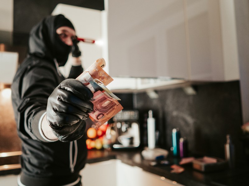 Ein Einbrecher hÃ¤lt Geldscheine in der Hand.