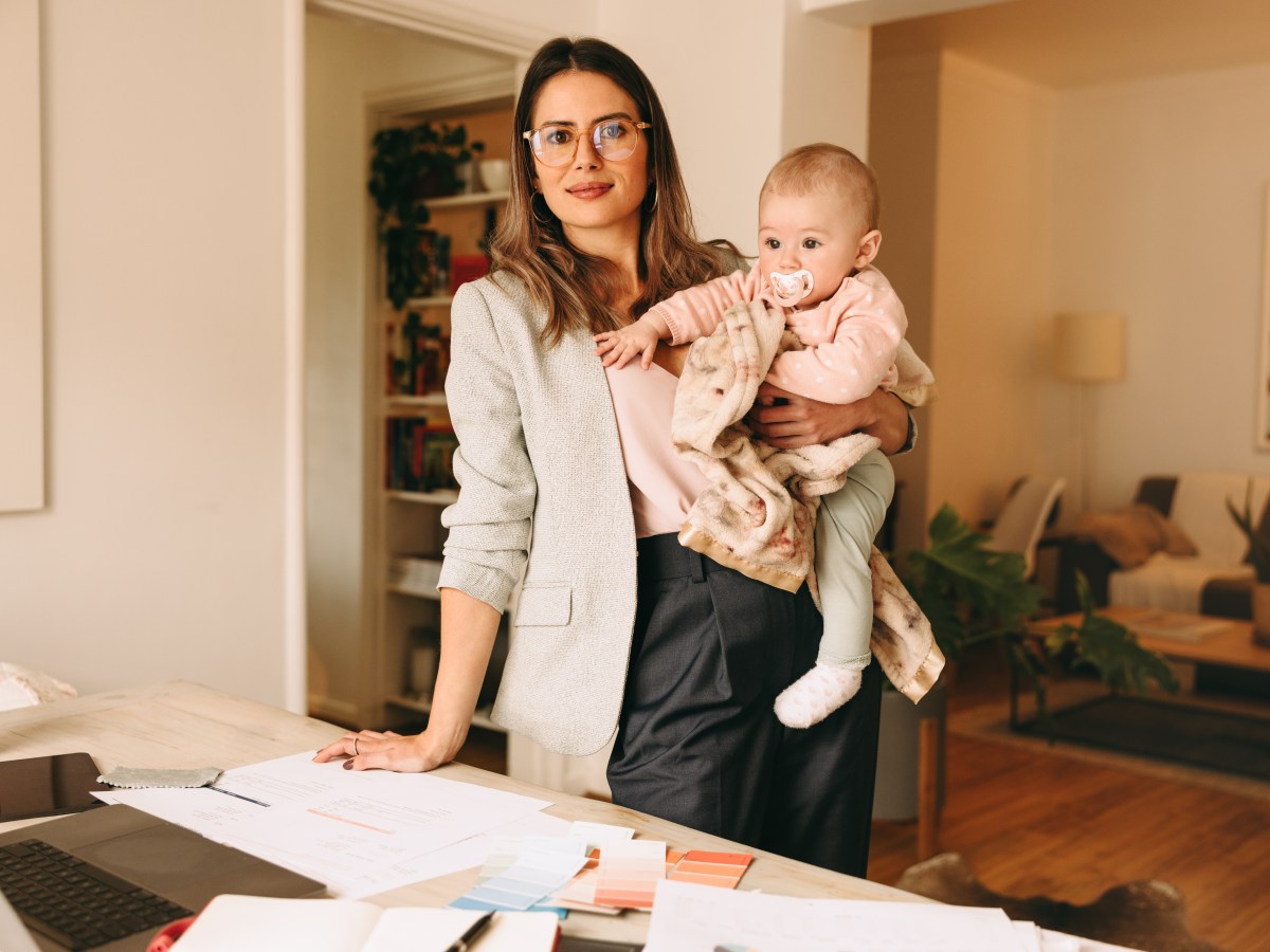 Eine Frau hÃ¤lt ein Baby auf dem Arm und steht vor einem Schreibtisch.