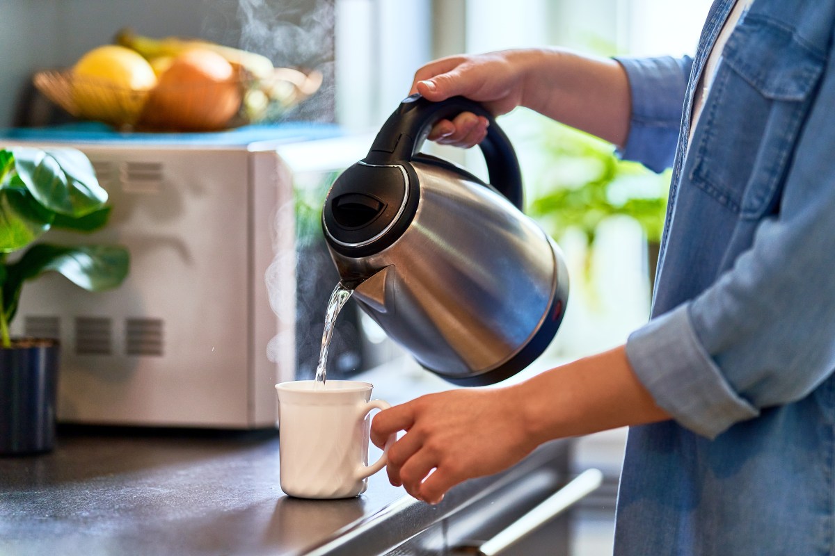 Person schüttet sich warmes Wasser in die Tasse.