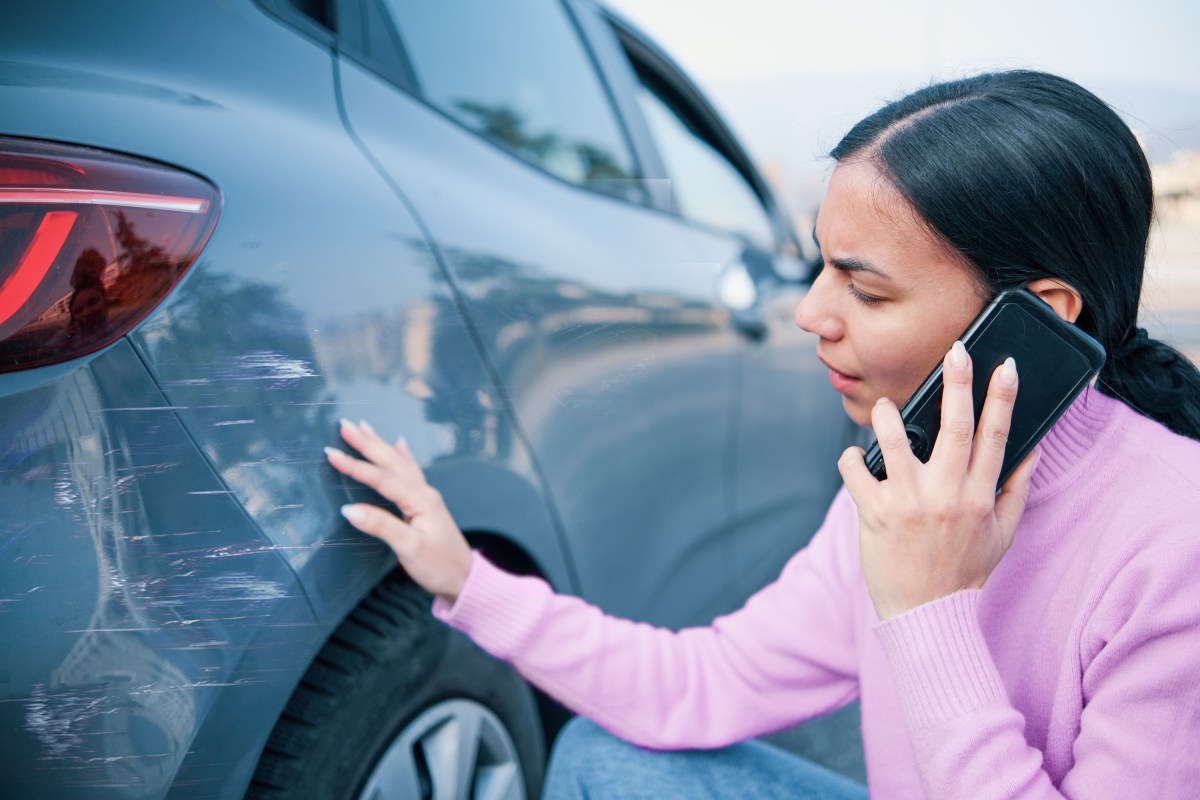 Frau telefoniert und schaut sich ihren Schaden am Auto an.