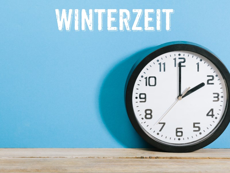 Eine Uhr steht auf einem Tisch. Über ihr steht die Aufschrift: Winterzeit.