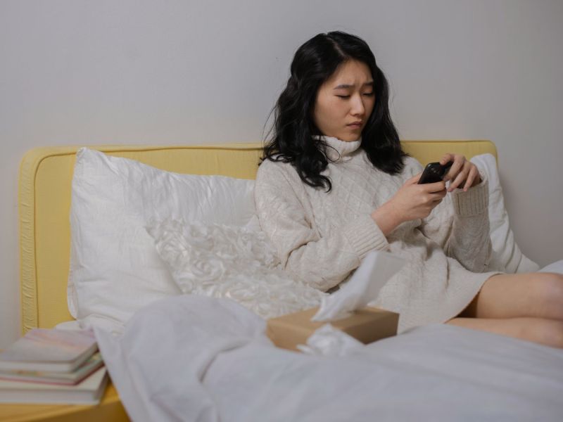 Frau liegt im Bett und schaut auf ihr Handy