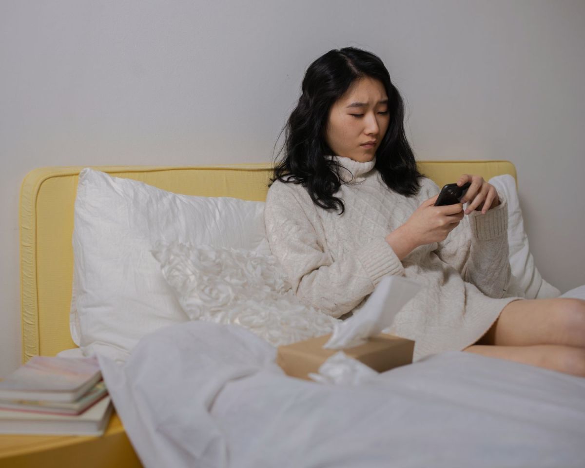 Frau liegt im Bett und schaut auf ihr Handy