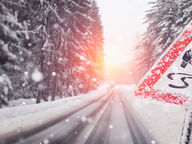 Eine Straße voller Schnee. Daneben steht ein Warnschild.