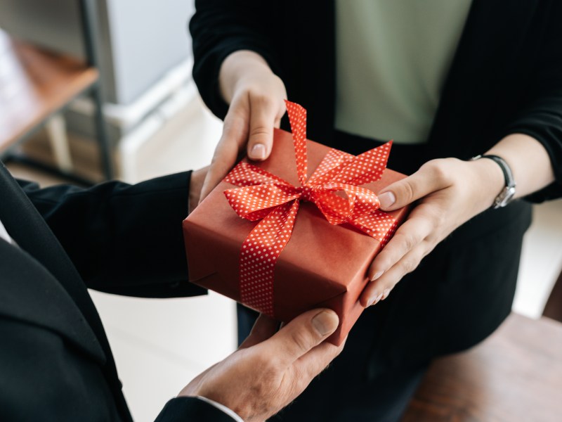 Eine Person übergibt ein Geschenk mit roter Schleife.