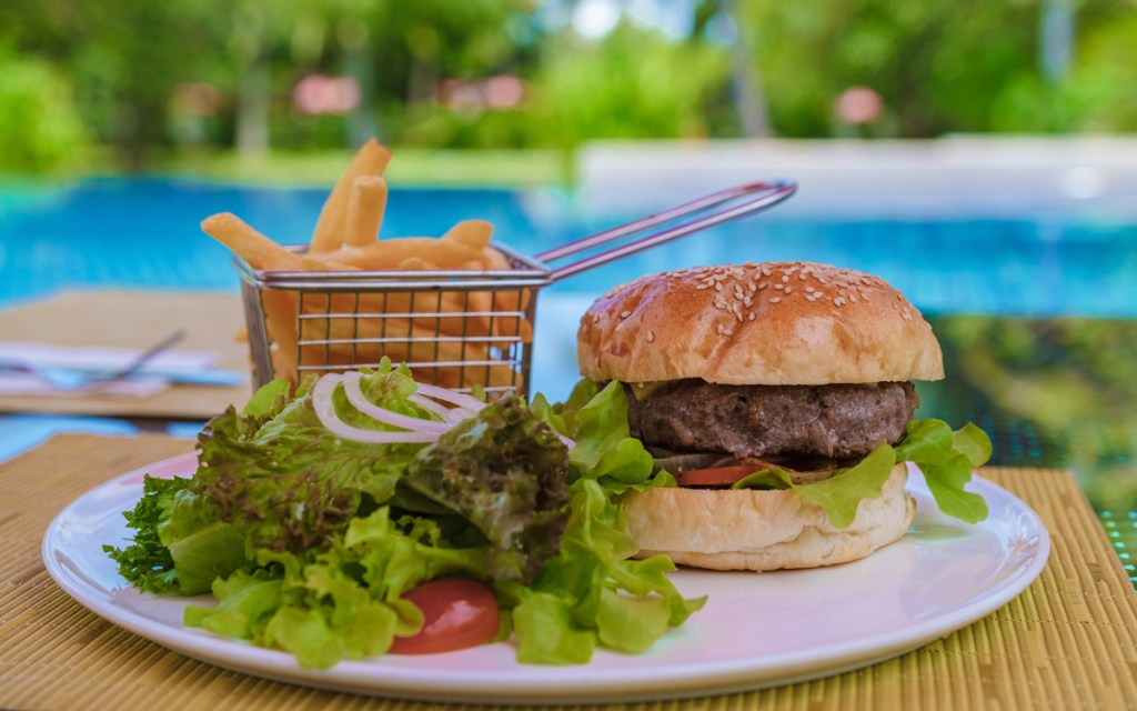 Ein Hamburger mit Pommes und Salat vor einem Schwimmbecken.