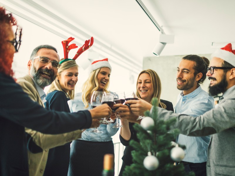 Eine Gruppe steht im BÃ¼ro und stÃ¶ÃŸt mit Wein an.