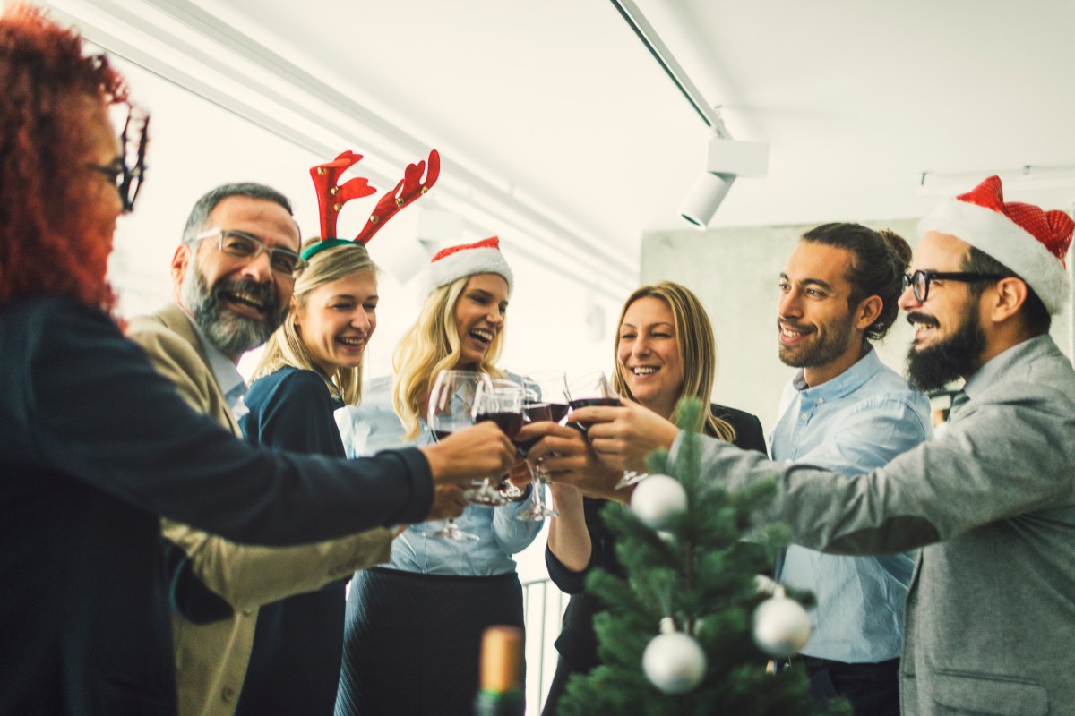 Eine Gruppe steht im Büro und stößt mit Wein an.