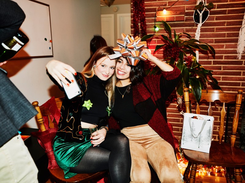 Lächelnde Freundinnen posieren für ein Selfie mit einer Schleife über dem Kopf während der Weihnachtsfeier.