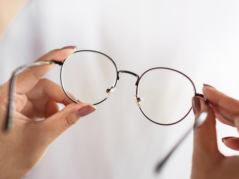 Eine Person hält eine Brille in der Hand.