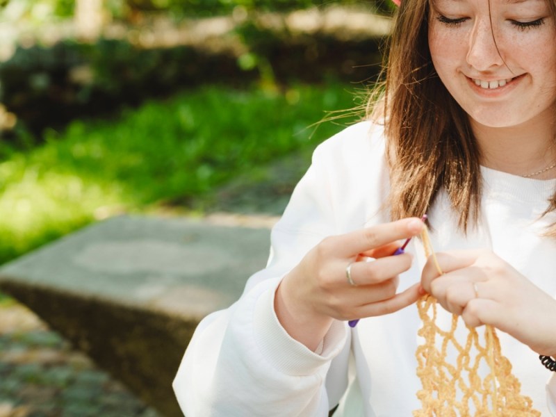 Eine junge Frau strickt im Grünen.