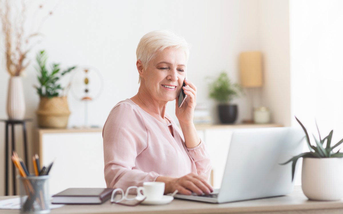 Eine ältere Dame sitzt am Laptop und telefoniert.