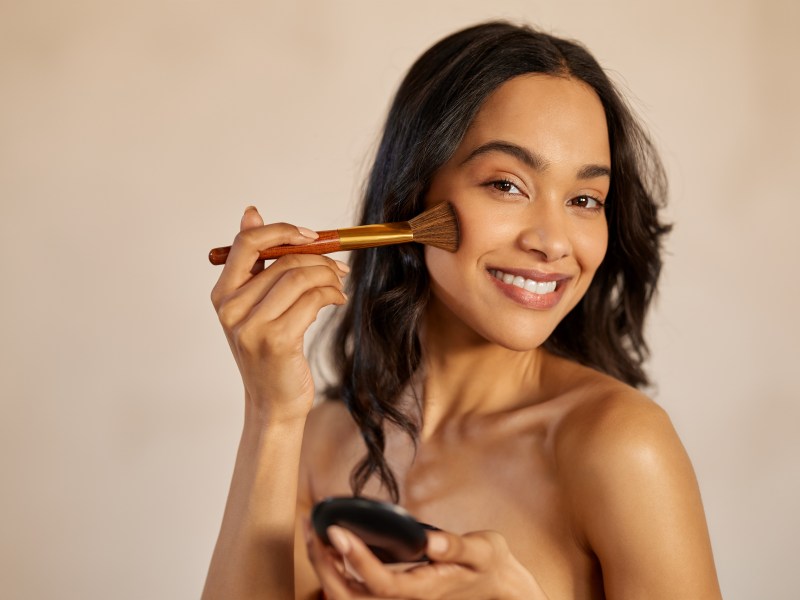 Frau trägt Contouring mit einem Pinsel auf ihre Wangen auf.