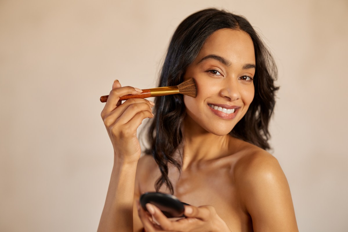 Frau trÃ¤gt Contouring mit einem Pinsel auf ihre Wangen auf.