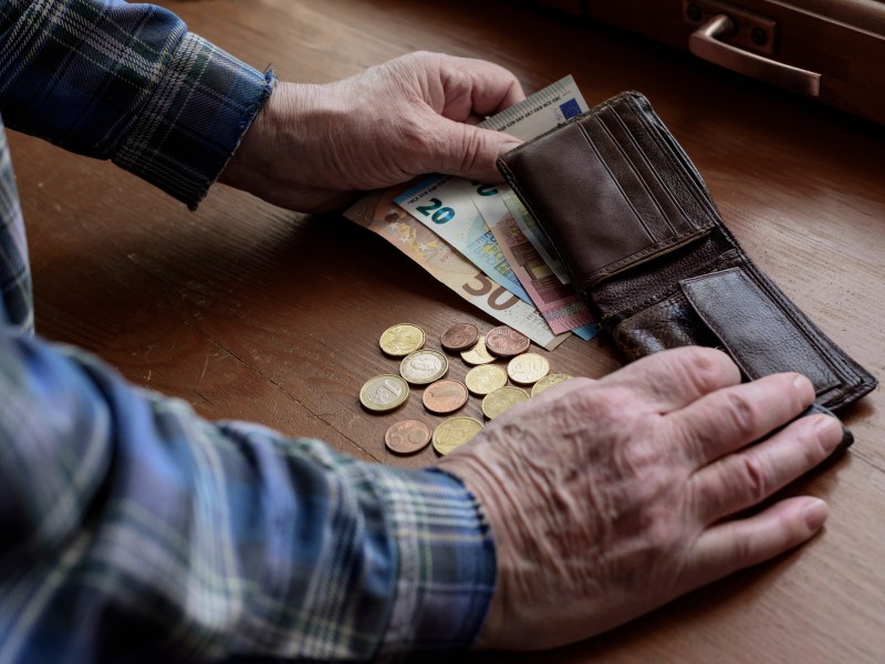 Ein Senior hat sein Portemonnaie geÃ¶ffnet. Davor liegen MÃ¼nzen und Geldscheine.