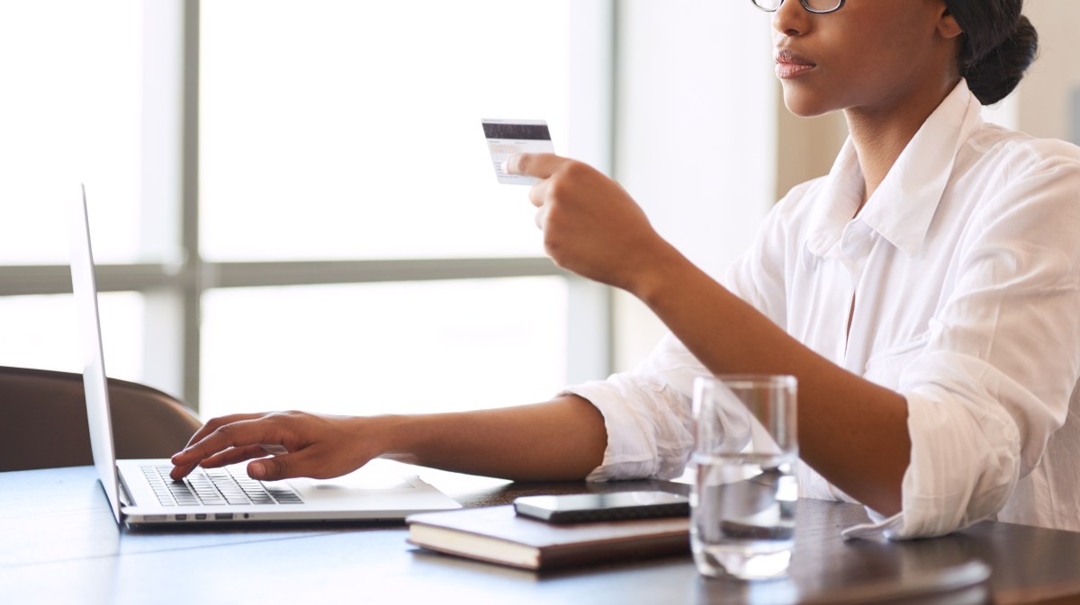 Eine Frau sitzt mit ihrer Bankkarte am Laptop.