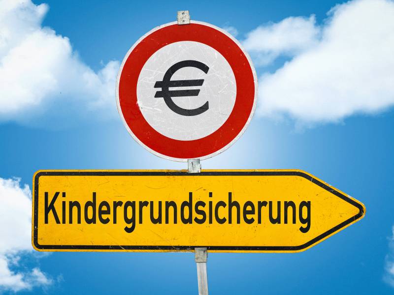 Auf einem gelben Schild steht das Wort "Kindergrundsicherung". Darüber ist ein rundes Schild mit einem Euro-Zeichen.