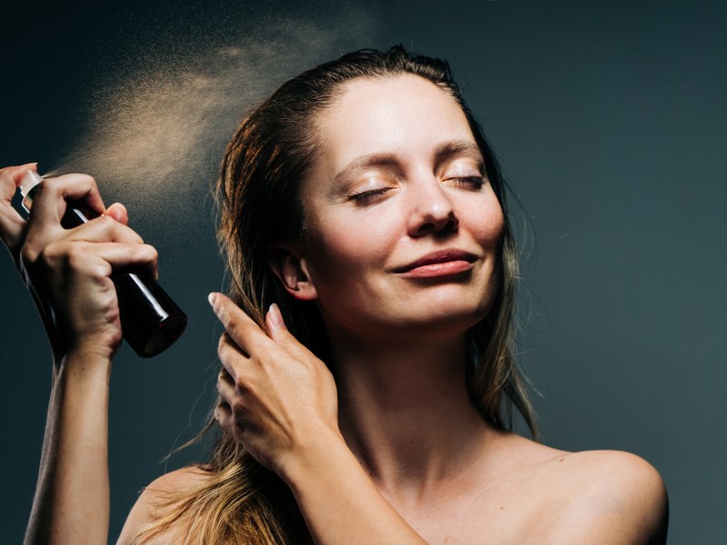 Frau sprüht Trockenshampoo