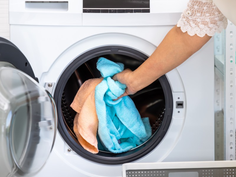 Eine Frau legt zwei Handtücher in die Waschmaschine.