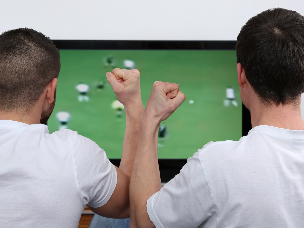 Zwei Männer stehen vor einem Fernseher und schauen Fußball.