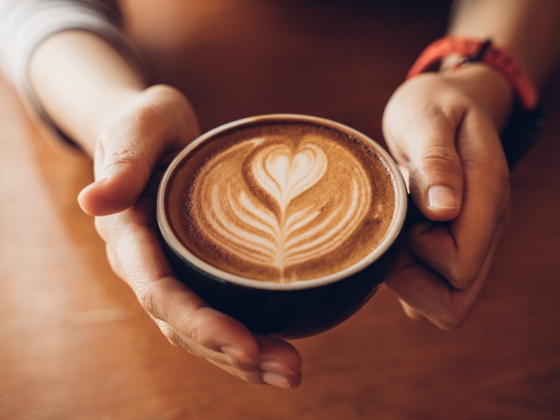 Eine Person hÃ¤lt einen Milchkaffee in der Hand.