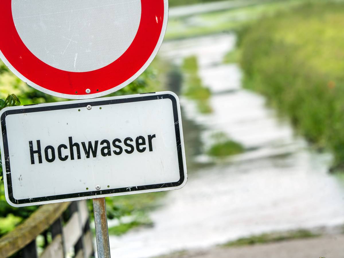 Auf einem Schild steht das Wort "Hochwasser". Dahinter ist ein gefluteter Weg.